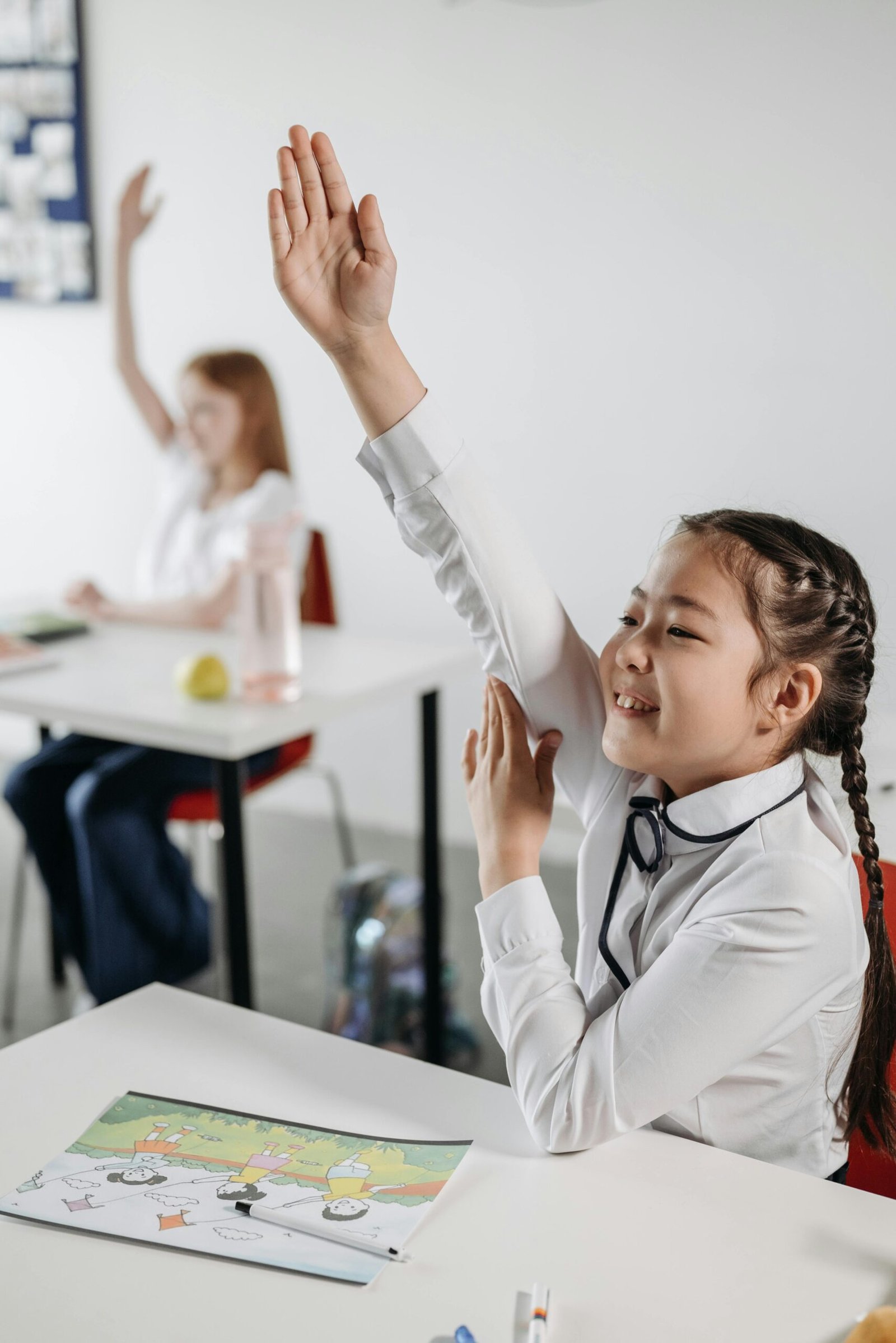 Two students actively participate in classroom with hands raised, eager to answer.
